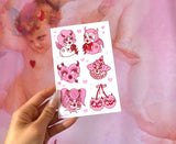 Vinyl Sticker sheet including 6 kitsch pink and red characters. It includes devil cherubs, a sexy rabbit, crying heart with and arrow through it, cherries with horns, and a femme clown