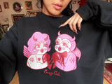Black cotton and polyester unisex crew neck sweat shirt featuring kitschy pink and white devil cherub and a red devil holding each side of a red broken heart.