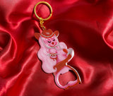 Metal keychain with gold key ring of a cowgirl with long pink hair wearing red wielding a pistol. The bottom is a a bottle opener
