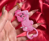 Metal keychain with gold key ring of a sexy pink poodle woman looking back. She has corset piercing on her back. The bottom is a bottle opener