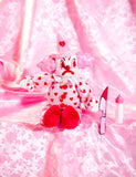 Pink and red clown doll with vinyl head and plush body. The pink jump suit has red broken gear pattern. The expression on the face is sad and crying 