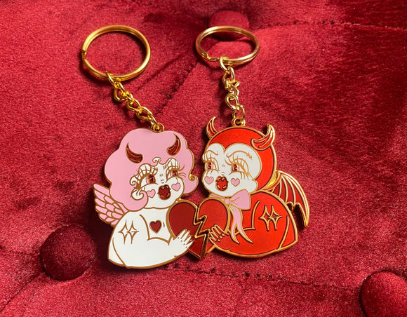Gold plated best friend keychains featuring a kitschy pink and white devil cherub and a red devil holding each side of a red broken heart