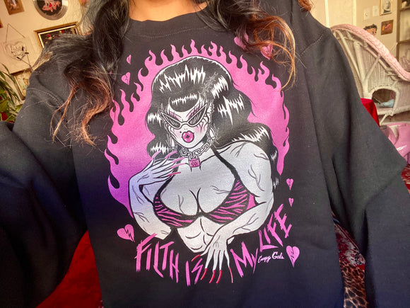 Unisex black cotton and polyester crew neck sweatshirt featuring a muscle lady with beehive hair and cat eye sunglasses surrounded by pink broken hearts with the words “Filth is My Life” under her. And pink flames in the background 